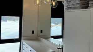 Ein modernes Badezimmer mit Holzboden, einem großen Spiegel, einem Waschbecken und einem Fenster mit Blick auf eine verschneite Landschaft.