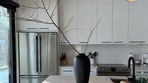 Eine moderne Küche mit weißen Schränken, Edelstahlgeräten, einer Holzbalkendecke und einer Essecke mit Tisch für zwei Personen.