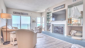 Un salon spacieux doté d’une cheminée, d’un téléviseur et d’une grande fenêtre donnant sur la plage.
