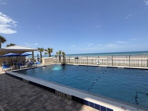 Uma piscina com posto de salva-vidas, espreguiçadeiras e vista para a praia.