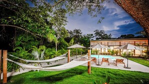 A pool area with a hammock, lounge chairs, and a building with large windows.