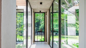 A modern corridor with glass walls and a view of a lush garden.