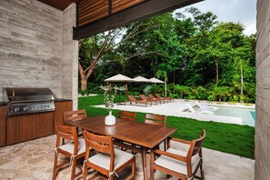 Un patio al aire libre con mesa y sillas de madera, una parrilla y una piscina.