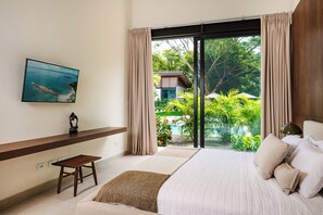 Un dormitorio con una cama grande, un televisor en la pared, una mesita pequeña y vistas a una piscina y zonas verdes.