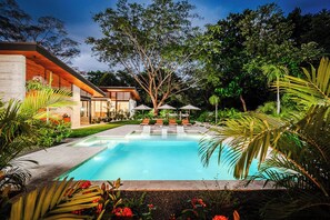 Un área de piscina moderna con una pileta cristalina, rodeada de exuberante vegetación y una terraza de madera.