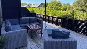 A deck with wicker furniture, a table, and a large umbrella. - Paradis på Sørlandet 2 (Agder)
