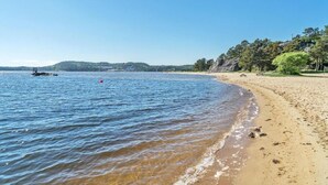 A beach with clear blue water, a sandy shore, and a boat in the distance. - Paradis på Sørlandet 2 (Agder)
