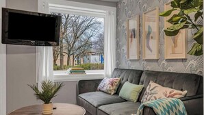 A living room with a grey sofa, a round wooden table, a potted plant, and a mounted TV.