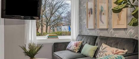 A living room with a grey sofa, a round wooden table, a potted plant, and a mounted TV.