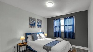 Un dormitorio con una cama, dos lámparas fijadas a la pared, una ventana con cortinas azules y dos cuadros de ciervos en la pared.