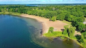 Vista aérea de una zona costera con playa arenosa, vegetación densa y un lago azul cristalino.