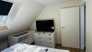 A bedroom with a bed, a crib, a television on a dresser, and a door.