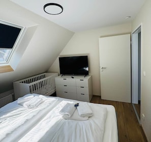 A bedroom with a bed, a crib, a television on a dresser, and a door.