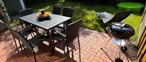 Une terrasse extérieure avec une table et des chaises, un barbecue et un espace abrité.