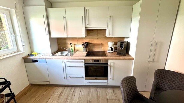 A compact kitchen with white cabinets, a built-in oven, a coffee maker, and a sink.