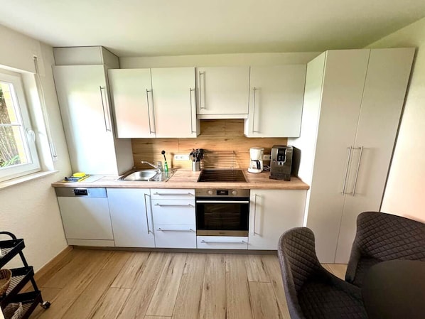 A compact kitchen with white cabinets, a built-in oven, a coffee maker, and a sink.