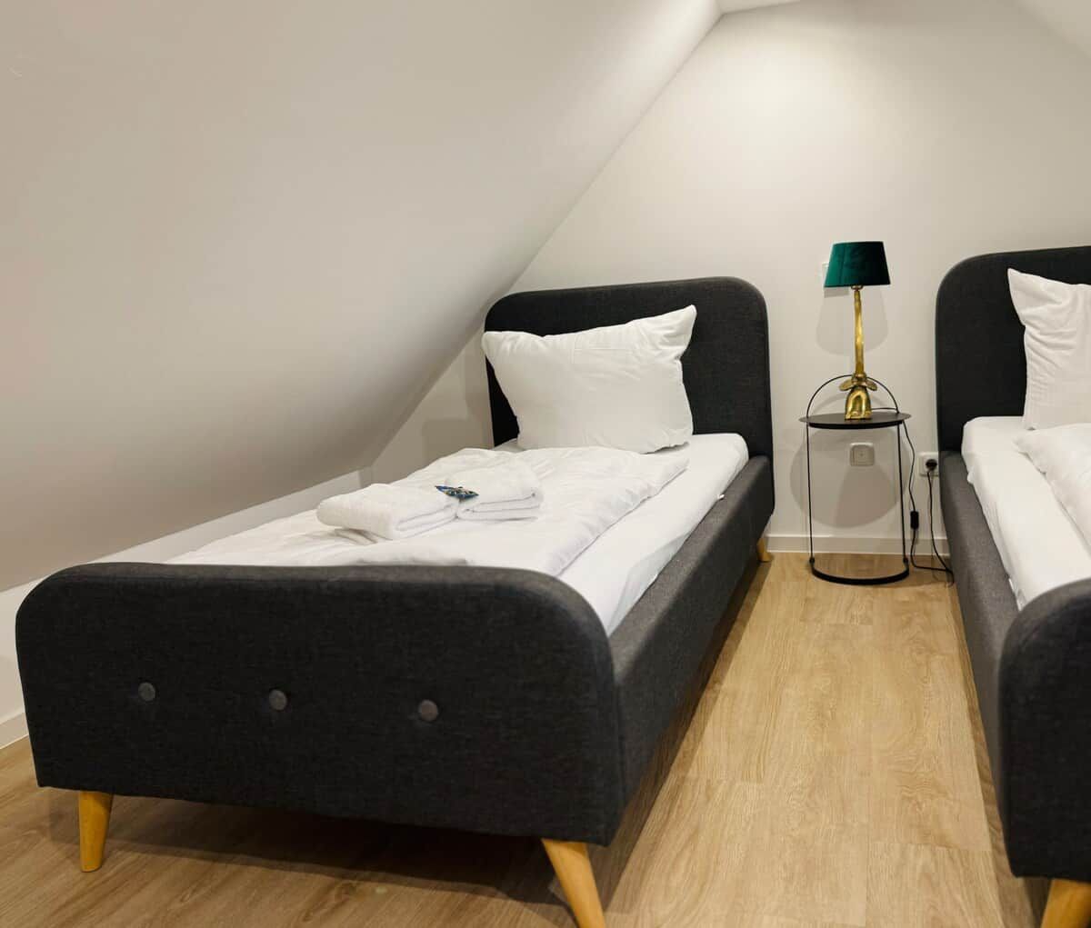 Une petite chambre moderne avec deux lits simples, une table de chevet avec une lampe et un plancher en bois.