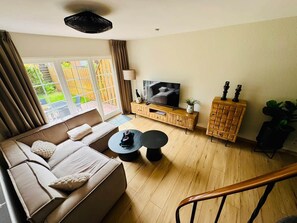 Una sala de estar moderna con un sofá, dos mesas auxiliares, un televisor y un aparador de madera.