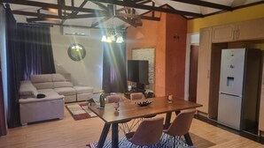 En moderne stue med sofa, spisebord med stole, fjernsyn og køleskab.