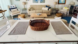 A living room with a wooden ceiling fan, a beige sofa, a coffee table, and a dining table with a wicker basket.