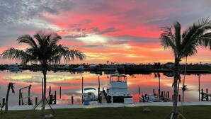A marina with boats docked, palm trees, and a sunset over the water.