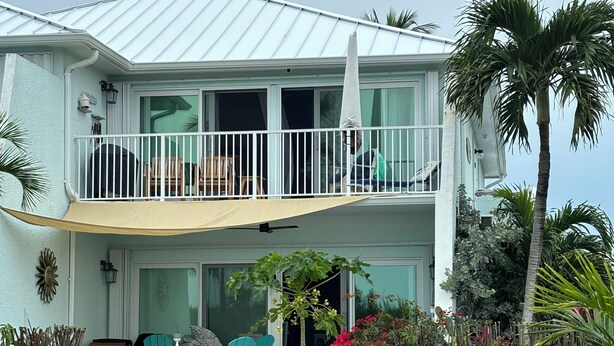 A two-story house with a balcony, outdoor seating, and tropical plants.