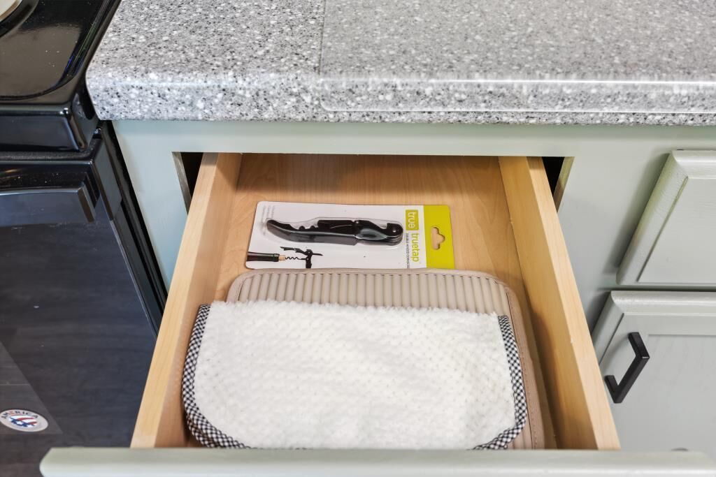 Eine Schublade mit einem weißen Geschirrtuch und einem schwarzen Küchenutensilien-Set.