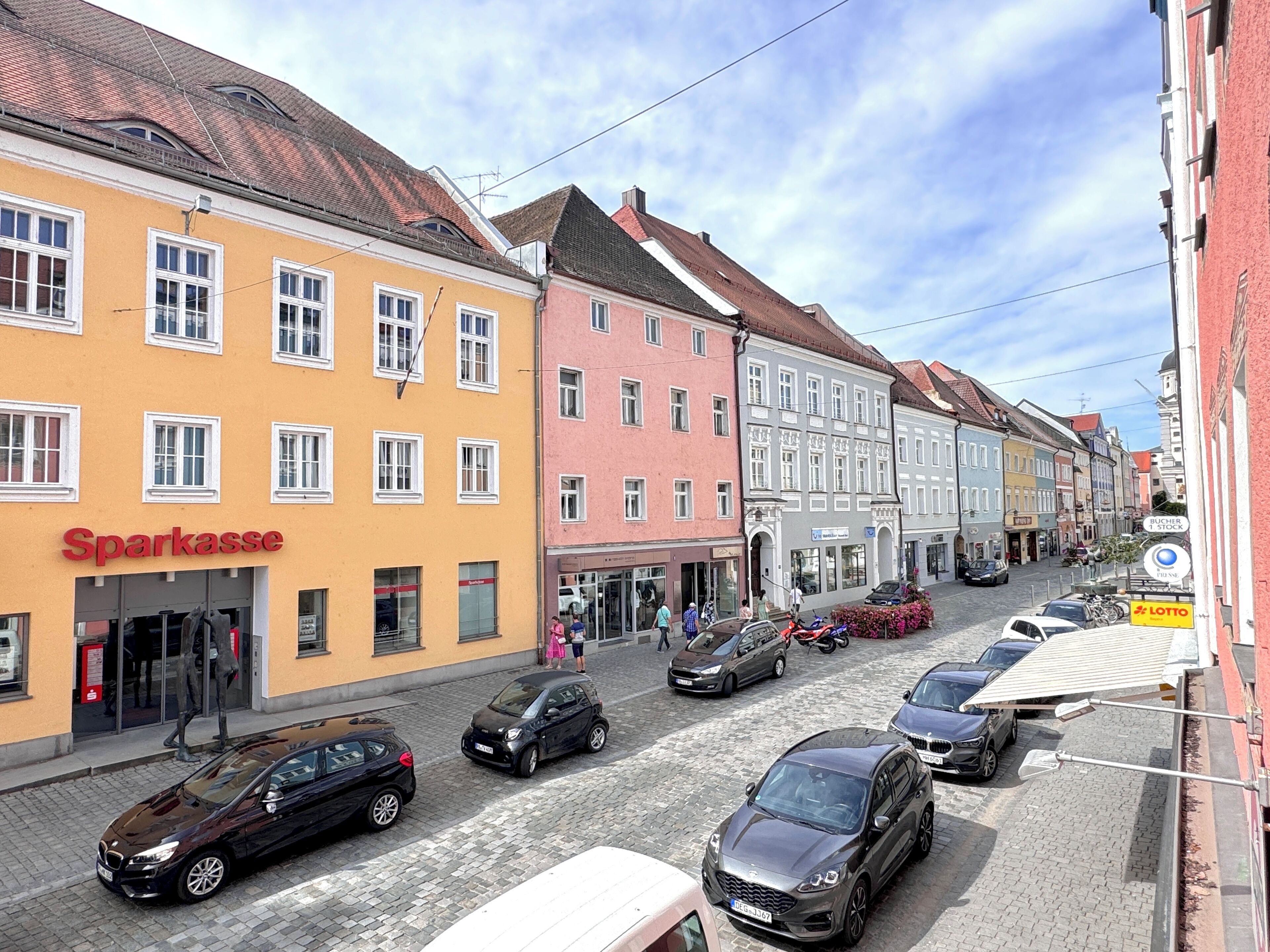 A street view with a yellow building labeled "Sparkasse" and a row of parked cars.