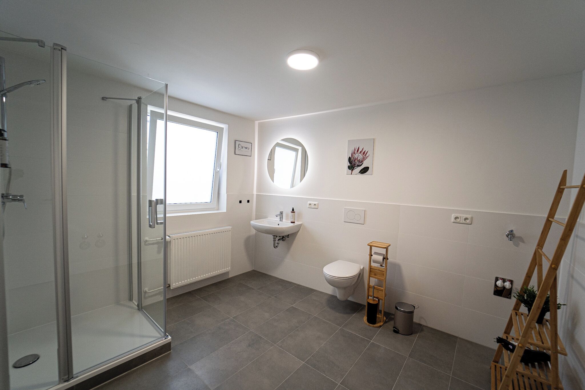 A modern bathroom with a glass shower enclosure, a sink, a toilet, and a wooden rack.