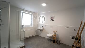 A modern bathroom with a glass shower enclosure, a sink, a toilet, and a wooden rack.
