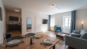 Un salon moderne avec un coin repas, une cuisine à l’arrière-plan et une grande fenêtre avec des rideaux.