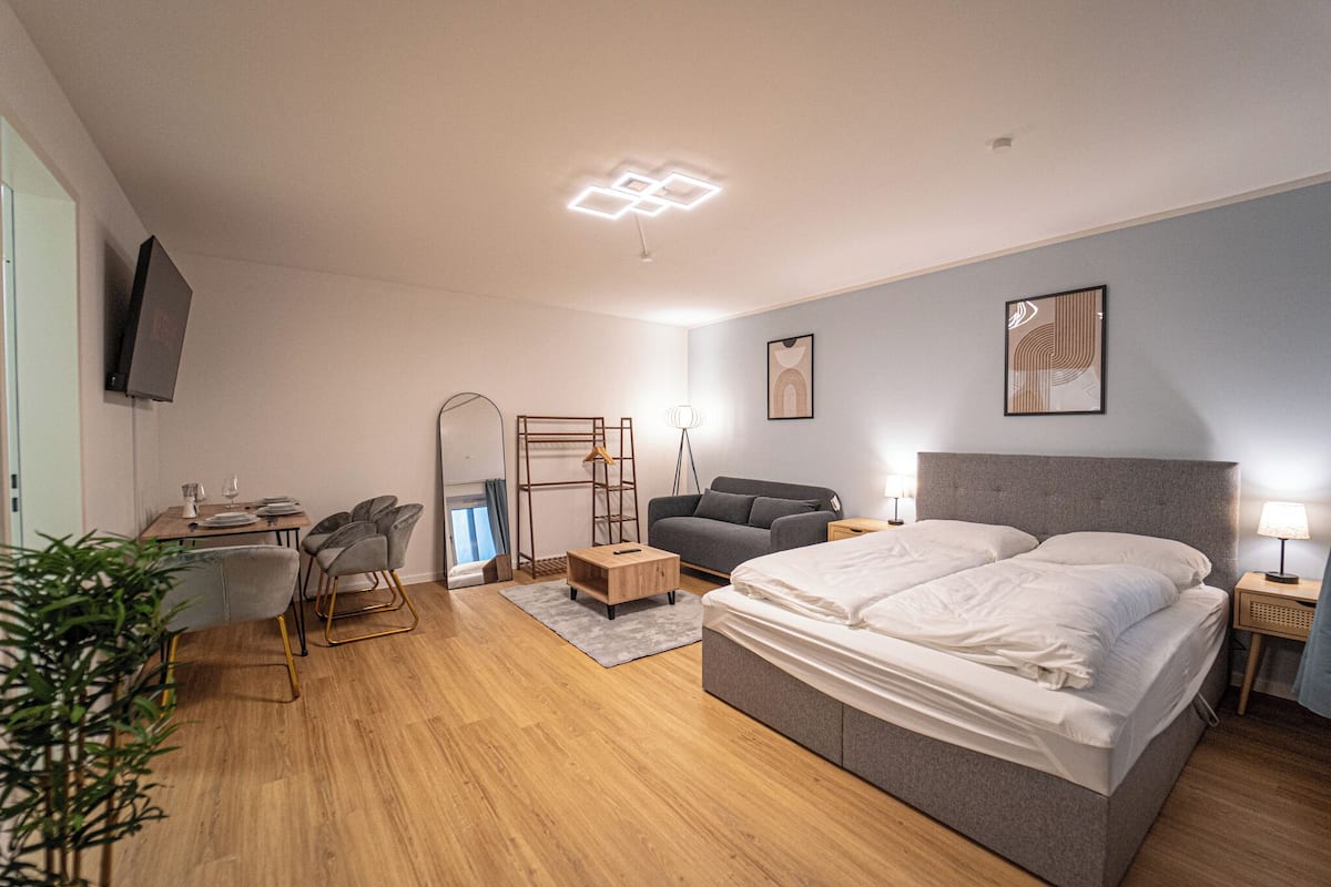 Een moderne hotelkamer met een groot bed, een bureau met stoel, een bank en een aan de muur bevestigde televisie.