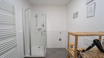 A modern bathroom with a glass-enclosed shower, a wooden drying rack, and a wall-mounted hairdryer.