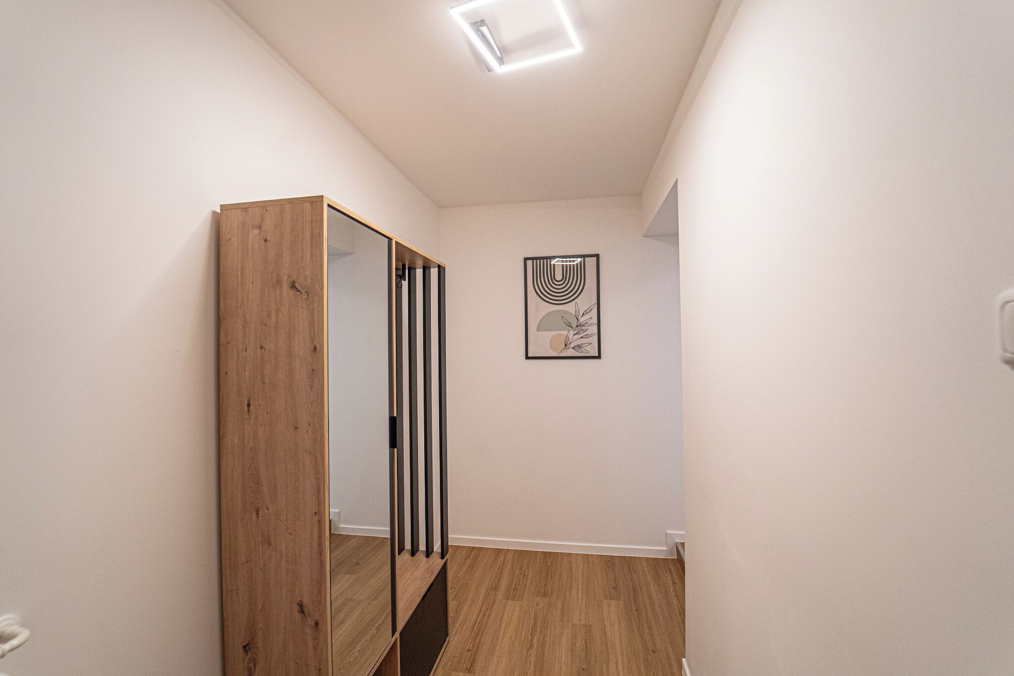 A hallway with a wooden wardrobe, a mirror, and a framed artwork on the wall.