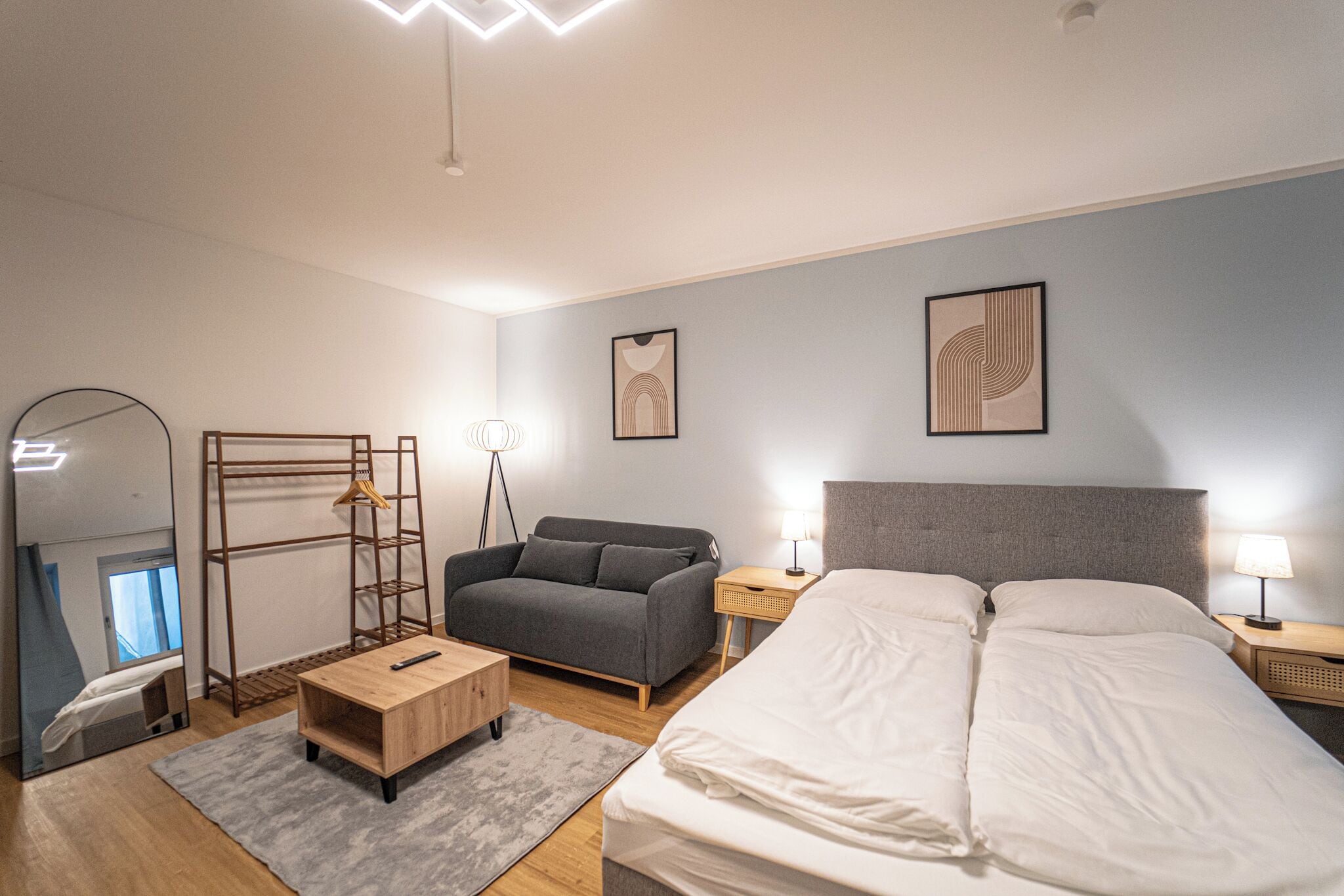 Une chambre d’hôtel moderne équipée d’un lit, d’un canapé, d’un bureau, d’un miroir et d’œuvres d’art accrochées aux murs.