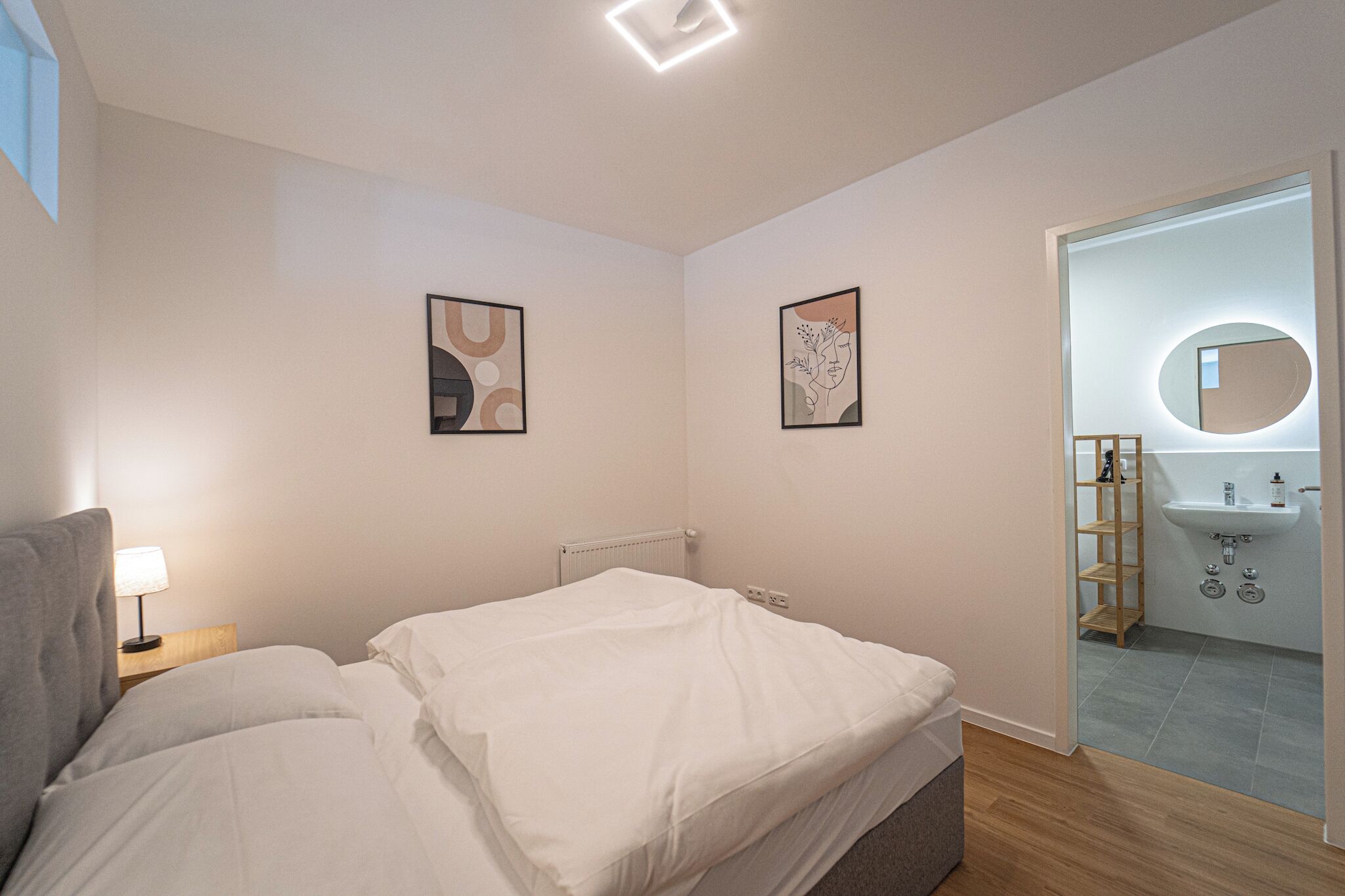 Un dormitorio con una cama, una lámpara de noche y dos obras de arte colgadas en la pared.