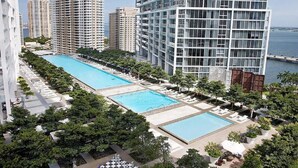 Un edificio de gran altura con una piscina en la azotea, rodeado de abundante vegetación y otros edificios altos.