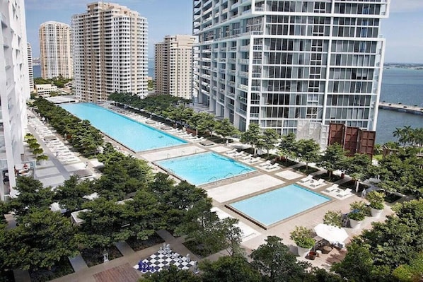 A high-rise building with two swimming pools surrounded by greenery and a view of the sea.