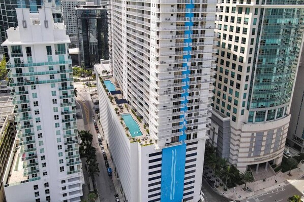 A high-rise hotel with multiple balconies, a rooftop pool, and a prominent blue stripe on the building.
