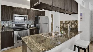 A modern kitchen with dark wood cabinets, stainless steel appliances, a granite countertop, and a small island with a sink. - Superb Private unit Perfectly Located In Brickell (Miami)