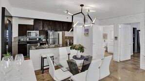 A modern kitchen with dark wood cabinets, a central island, and a dining area with a glass table and white chairs. - Superb Private unit Perfectly Located In Brickell (Miami)