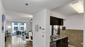 A modern kitchen with dark cabinets, a tiled backsplash, and a dining area with a glass door leading to a balcony. - Superb Private unit Perfectly Located In Brickell (Miami)