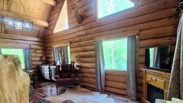 Interior de una cabaña de troncos con sofá, televisión y piso de madera.
