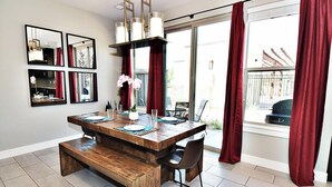 Un coin repas avec une table en bois, des chaises et un banc. Il y a quatre miroirs au mur, un chandelier et un vase avec des fleurs.