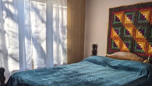A bedroom with a bed, a quilt, a window with curtains, and a wall with a quilt hanging. - Enjoy the natural splendor and outdoor thrills in the quaint town of Lupton, MI. (Lupton)
