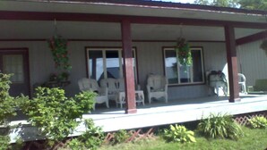 A covered porch with white chairs and hanging plants. - Enjoy the natural splendor and outdoor thrills in the quaint town of Lupton, MI. (Lupton)