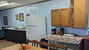 A compact kitchen with wooden cabinets, a refrigerator, and a dining table set with orange napkins and a decorative centerpiece. - Enjoy the natural splendor and outdoor thrills in the quaint town of Lupton, MI. (Lupton)