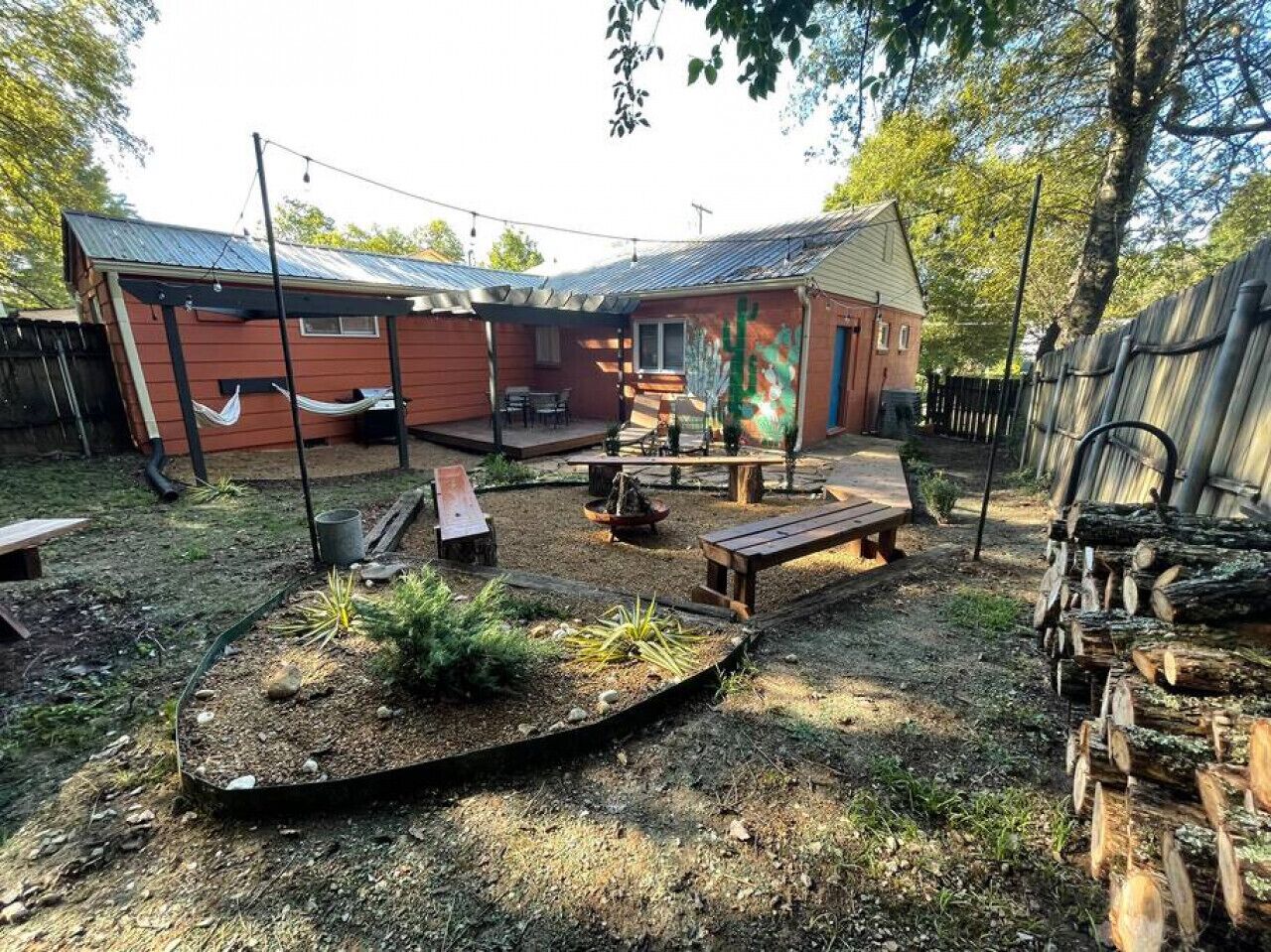 A backyard with a wooden deck, a hammock, a fire pit, and a wooden bench.