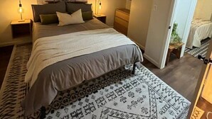 Un dormitorio con cama, ventilador de techo, mesita de noche, lámpara de pared y una puerta que da a otra habitación.