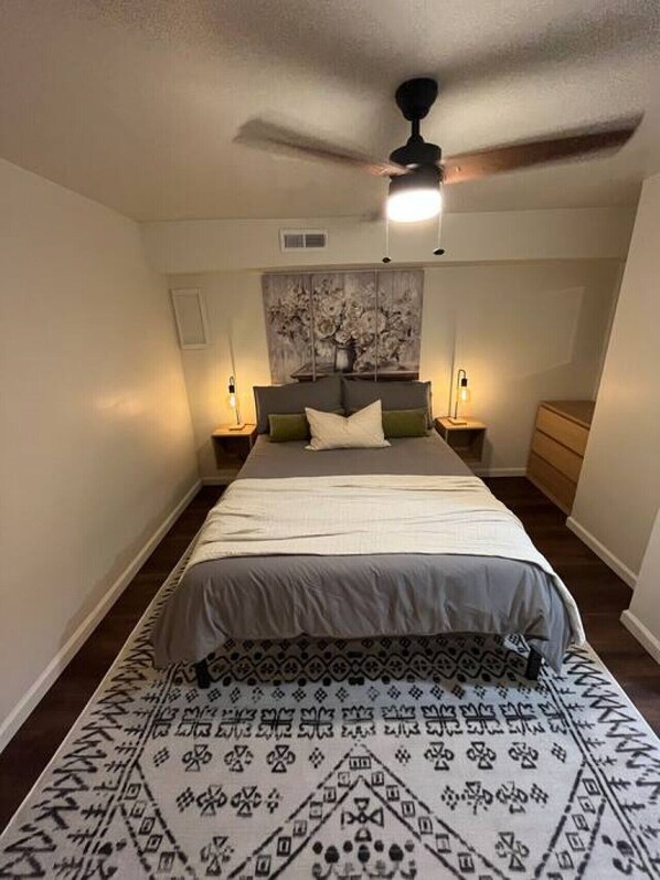 Un dormitorio con una cama, un ventilador de techo y una mesita de noche con una lámpara.